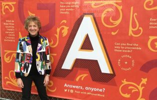 Ann Friedman standing in front of a construction fence at Planet Word decorated with a large letter A and riddles
