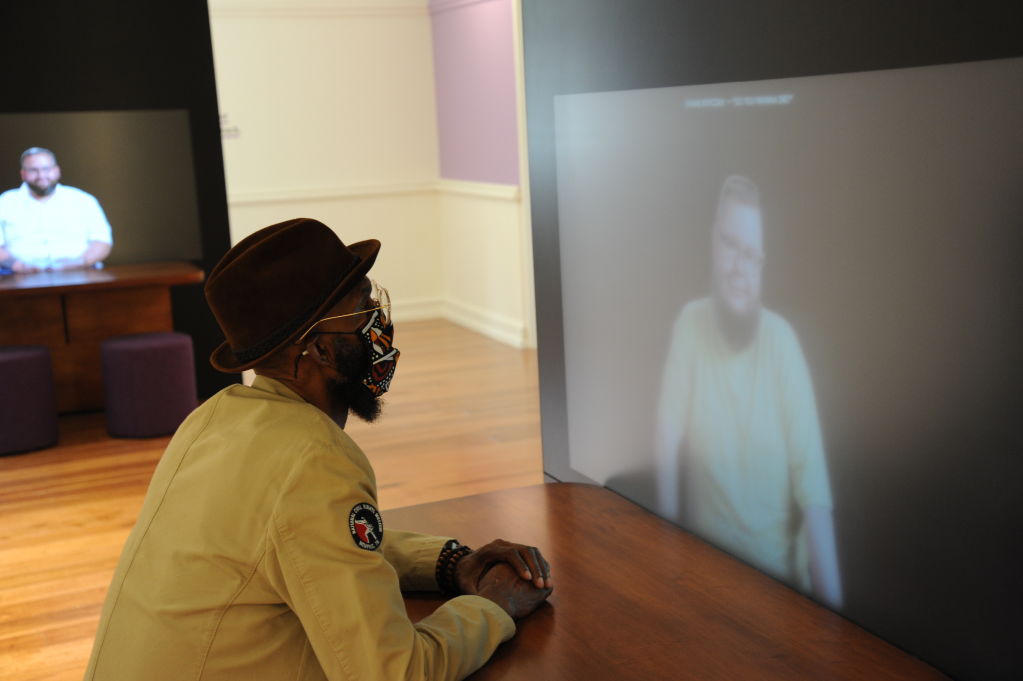 African American man in hat listening to a video essay in Words Matter gallery