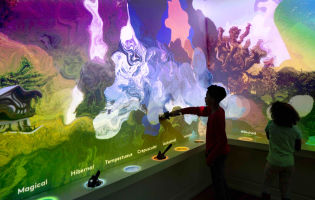 Two children in the Word Worlds exhibit at Planet Word. The wall is awash with swirls of color.