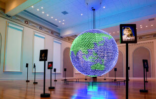A large blue and green LED globe in Planet Word's Spoken World gallery showing the Asian continent and Oceania. Standing tablets are placed around the room.